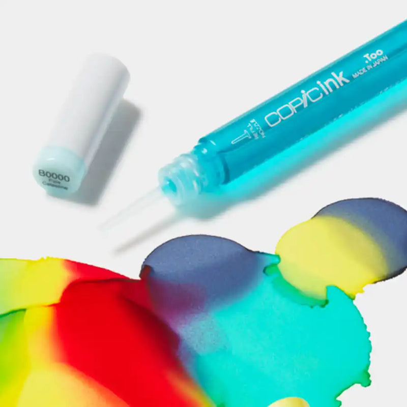 A blue translucent bottle of Copic ink with a dropper tip, next to a light blue cap, with multiple colors of ink spilled on a white surface.